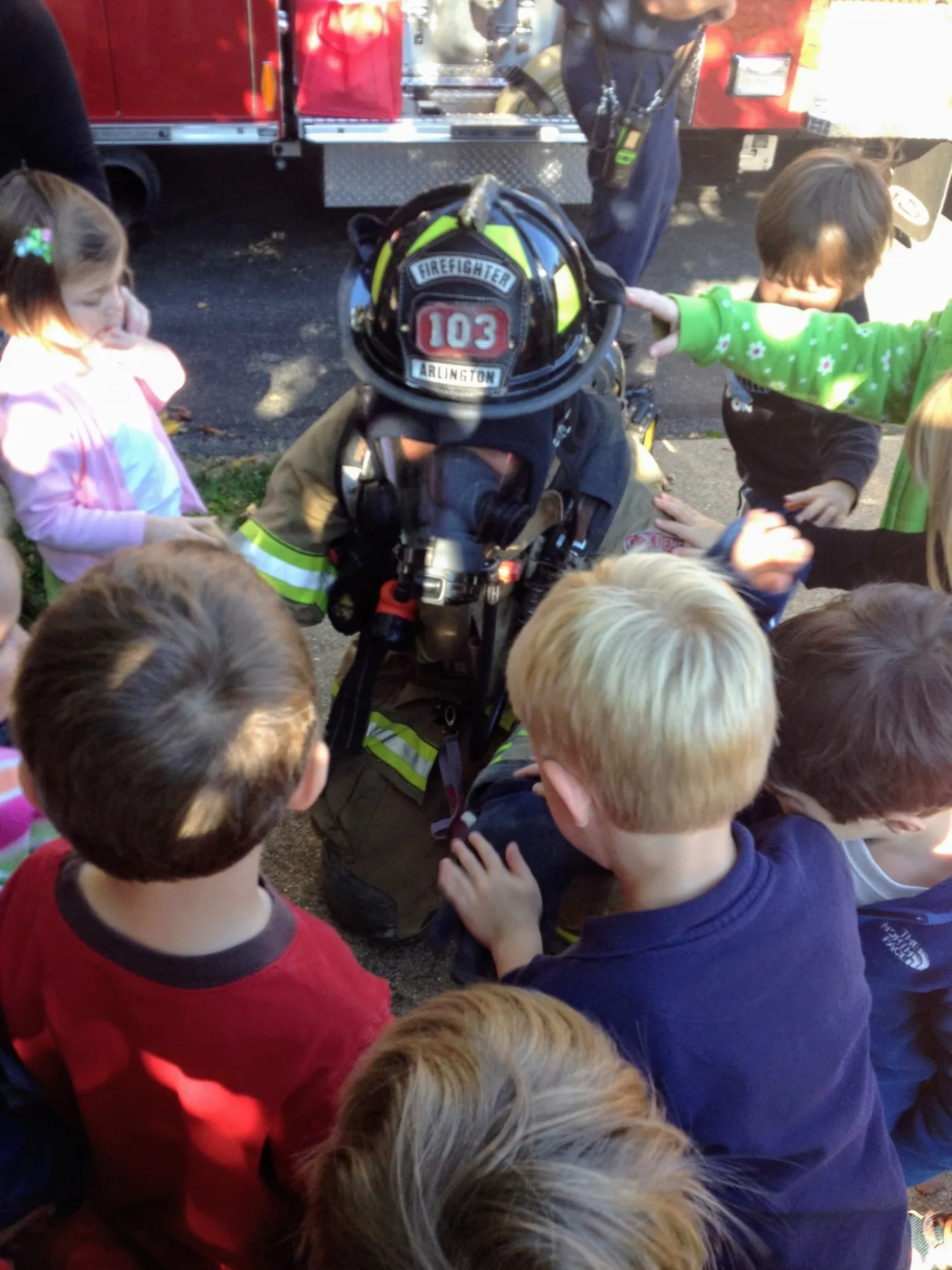 A firefighter in full gear and an air mask, surrounded by curious schoolchildren